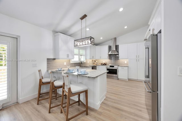 kitchen with pendant lighting, lofted ceiling, kitchen peninsula, wall chimney range hood, and appliances with stainless steel finishes