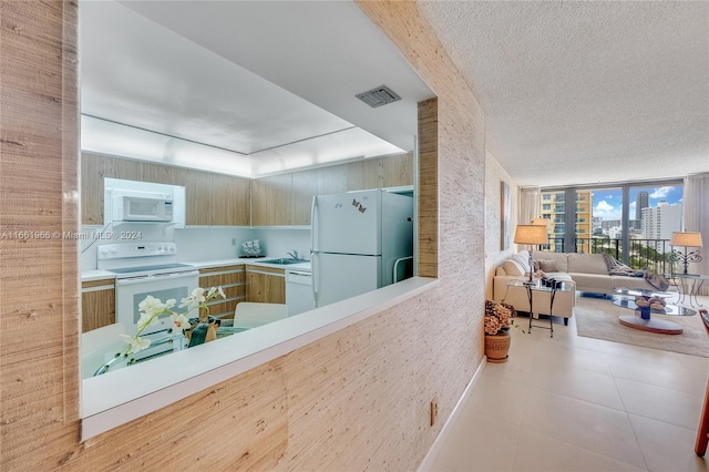 kitchen with a textured ceiling, light tile patterned flooring, sink, white appliances, and expansive windows