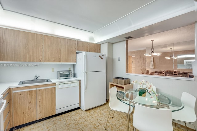 kitchen featuring white appliances, pendant lighting, light brown cabinetry, sink, and a chandelier