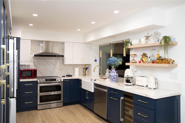 kitchen with appliances with stainless steel finishes, wine cooler, wall chimney exhaust hood, light stone countertops, and light wood-type flooring