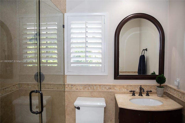 bathroom with tile walls, a shower with door, vanity, and toilet