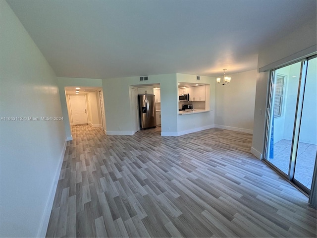 unfurnished living room featuring an inviting chandelier and light hardwood / wood-style flooring