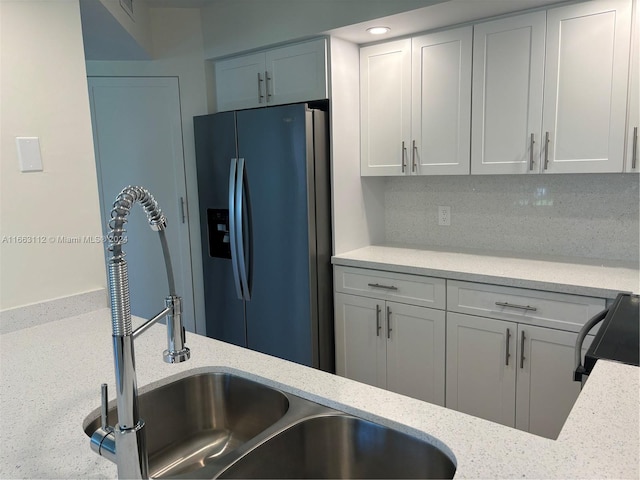 kitchen with light stone countertops, stainless steel fridge with ice dispenser, backsplash, stove, and white cabinets