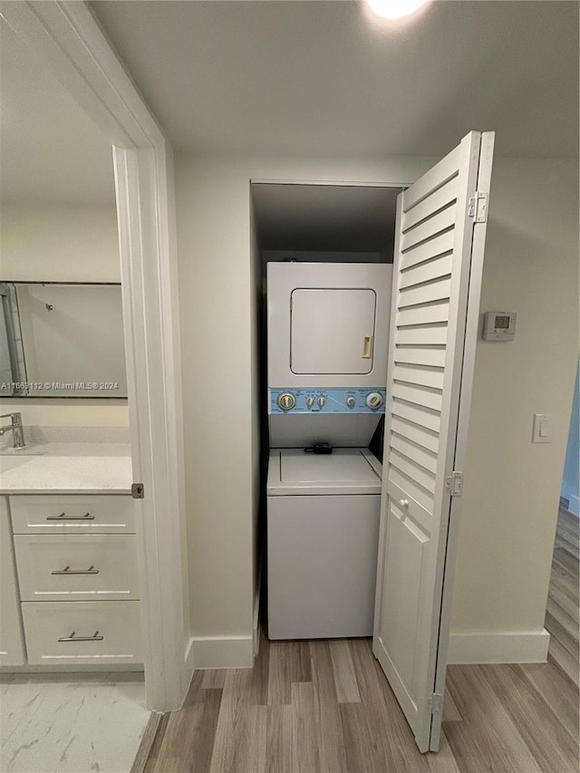 clothes washing area with stacked washer and clothes dryer and light wood-type flooring