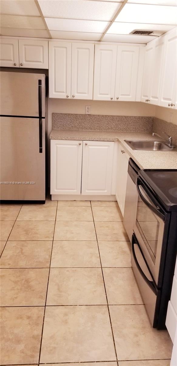 kitchen with stainless steel refrigerator, electric range oven, light tile patterned floors, and white cabinets