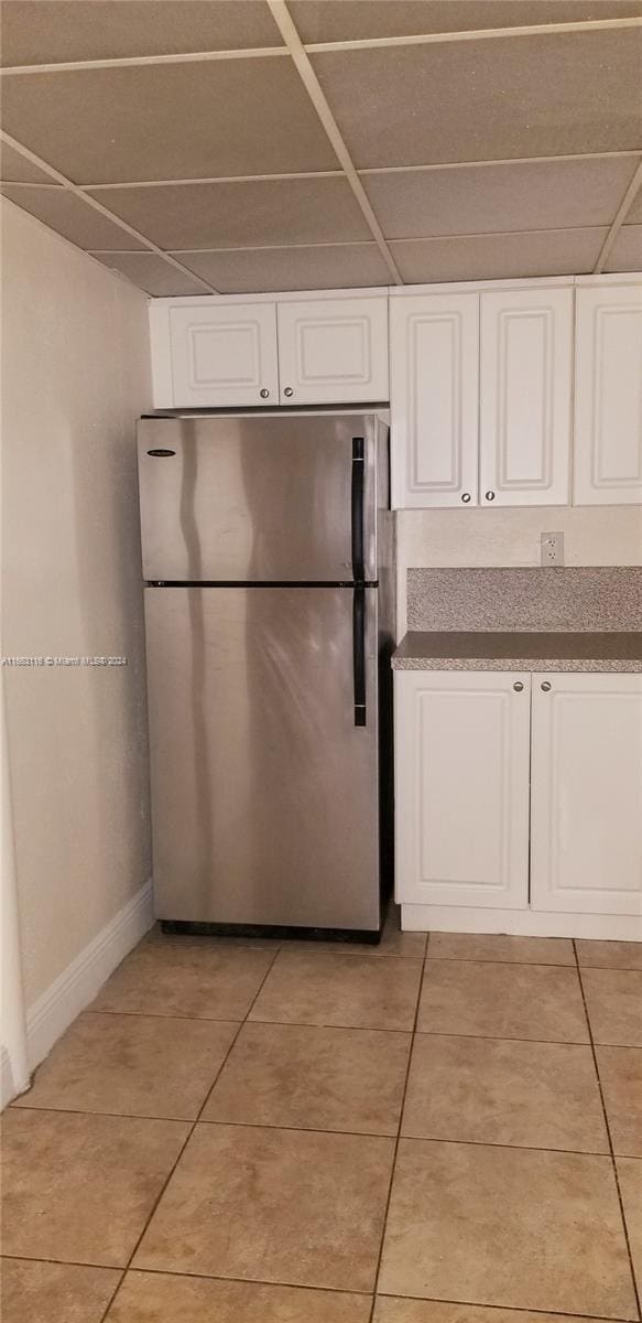 kitchen with stainless steel refrigerator, a drop ceiling, light tile patterned floors, and white cabinets