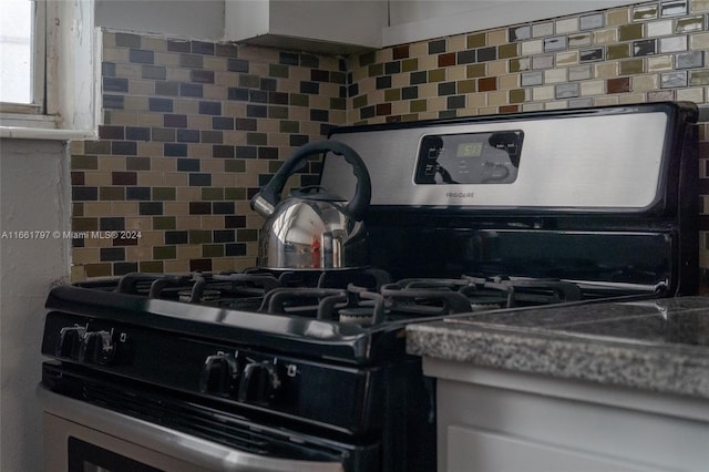 room details featuring stainless steel gas stove, stone counters, tasteful backsplash, and white cabinetry