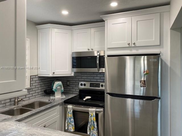 kitchen with light stone counters, stainless steel appliances, sink, and white cabinetry