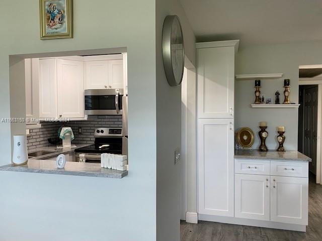 kitchen featuring stainless steel appliances, white cabinetry, hardwood / wood-style floors, and tasteful backsplash