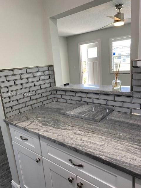 kitchen with light stone countertops, white cabinets, ceiling fan, and tasteful backsplash