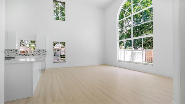 unfurnished living room featuring a high ceiling, light wood-type flooring, sink, and a wealth of natural light