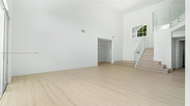 unfurnished living room featuring light hardwood / wood-style flooring and a towering ceiling