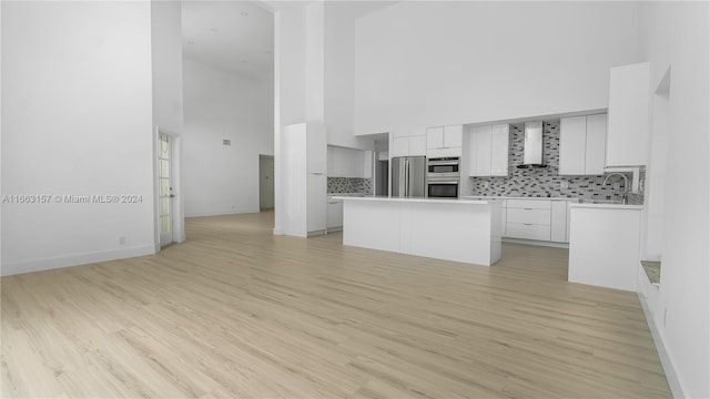 kitchen featuring a high ceiling, wall chimney exhaust hood, light wood-type flooring, and white cabinets