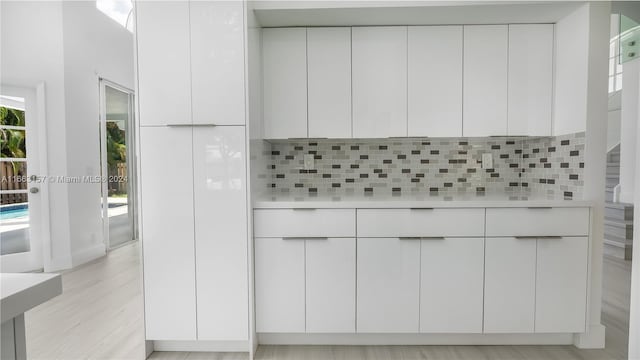 kitchen with backsplash, light hardwood / wood-style floors, and white cabinetry