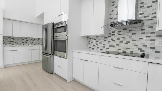 kitchen with light wood-type flooring, white cabinetry, wall chimney range hood, decorative backsplash, and stainless steel appliances