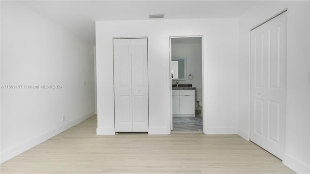 unfurnished bedroom with multiple closets, light wood-type flooring, and ensuite bathroom