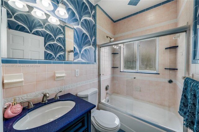 full bathroom with enclosed tub / shower combo, tile walls, vanity, and toilet