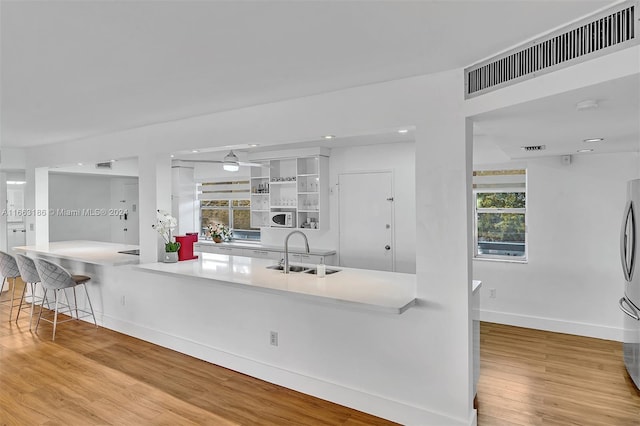 kitchen with white cabinetry, kitchen peninsula, a breakfast bar area, light wood-type flooring, and sink