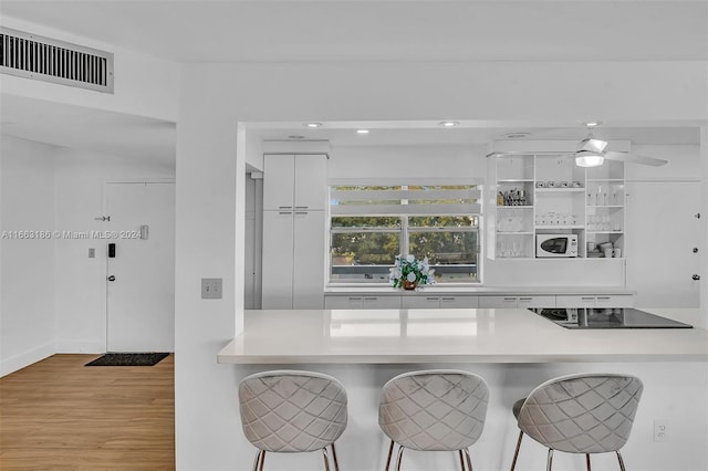 kitchen featuring black electric stovetop, white cabinets, light hardwood / wood-style floors, and a breakfast bar area