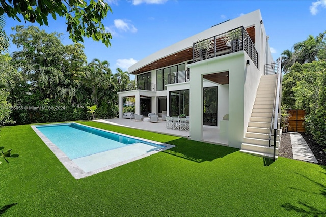 rear view of property with a balcony, a patio, ceiling fan, and a yard