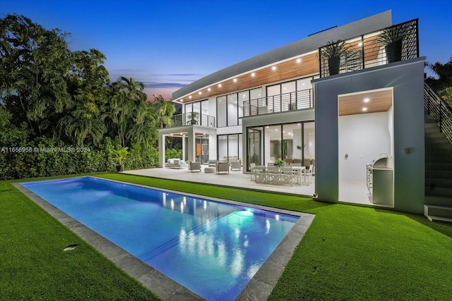 back house at dusk with a balcony, a fenced in pool, a yard, and a patio