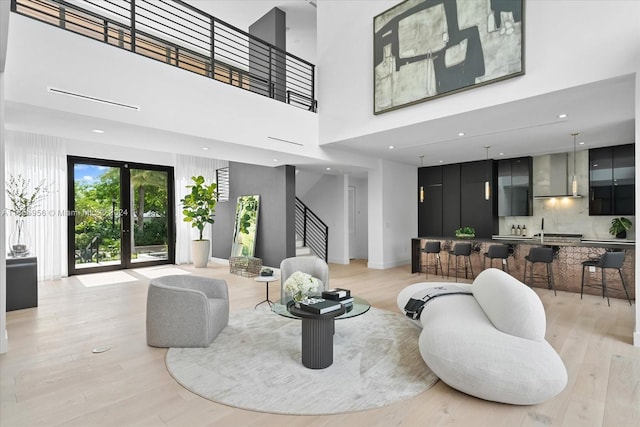 living room featuring light wood-type flooring, a high ceiling, french doors, and sink