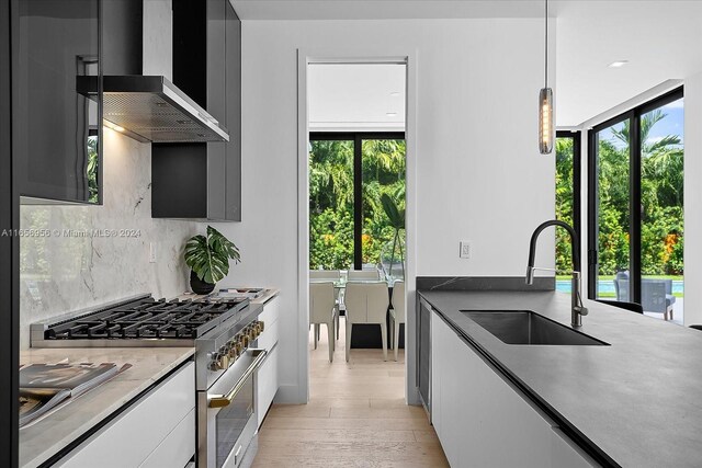 kitchen featuring hanging light fixtures, high end stainless steel range, light hardwood / wood-style flooring, sink, and wall chimney range hood