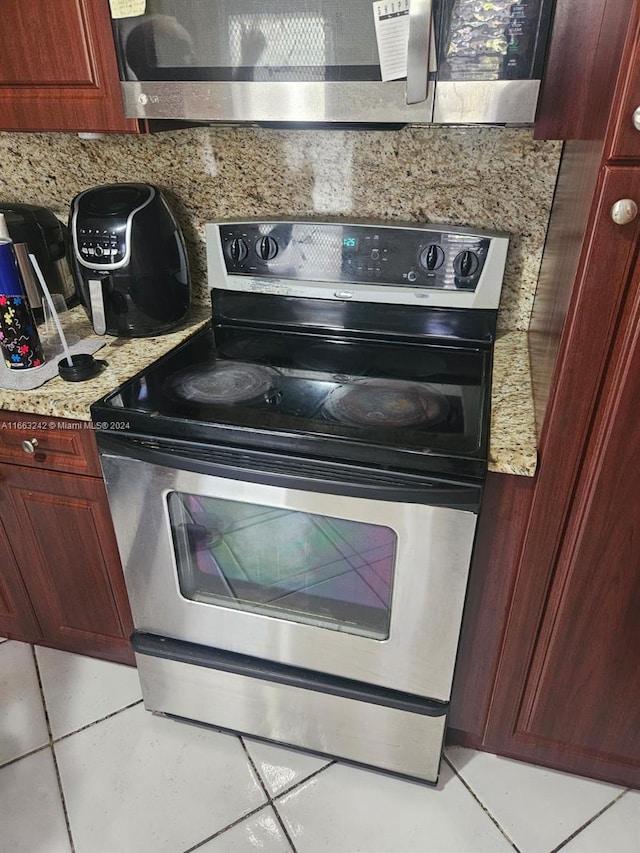 kitchen with appliances with stainless steel finishes, light tile patterned floors, and light stone counters