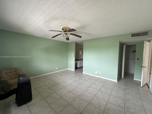 empty room with ceiling fan, light tile patterned floors, and a textured ceiling