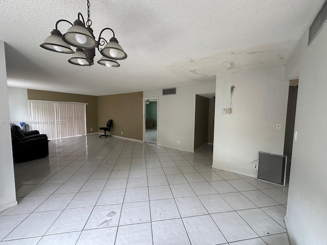 empty room with a textured ceiling, a chandelier, and light tile patterned flooring