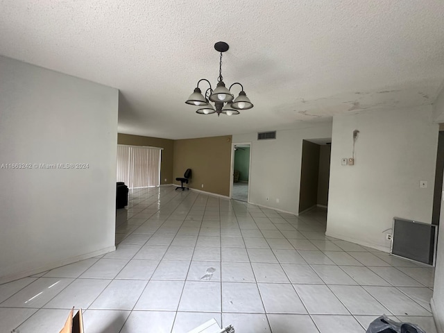 tiled empty room with a textured ceiling and a notable chandelier