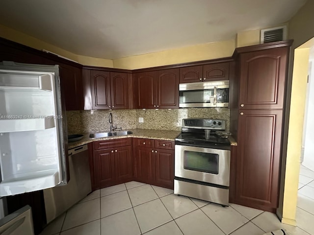 kitchen with sink, backsplash, appliances with stainless steel finishes, light tile patterned floors, and light stone countertops