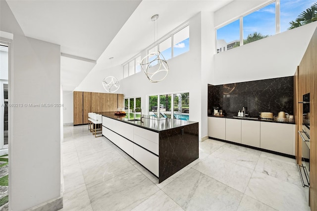 kitchen featuring sink, tasteful backsplash, decorative light fixtures, stainless steel oven, and a high ceiling