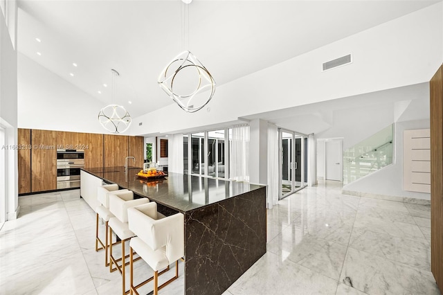 kitchen with hanging light fixtures, a large island, high vaulted ceiling, a kitchen breakfast bar, and an inviting chandelier