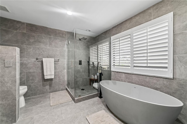 bathroom featuring plus walk in shower, tile walls, tile patterned floors, and toilet