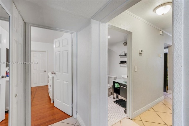 hallway featuring a textured ceiling, light tile patterned flooring, and crown molding