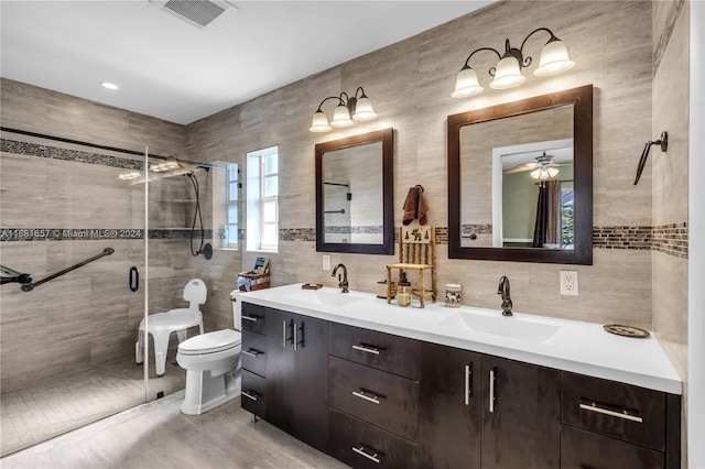 bathroom with tile walls, a shower with door, ceiling fan, vanity, and toilet