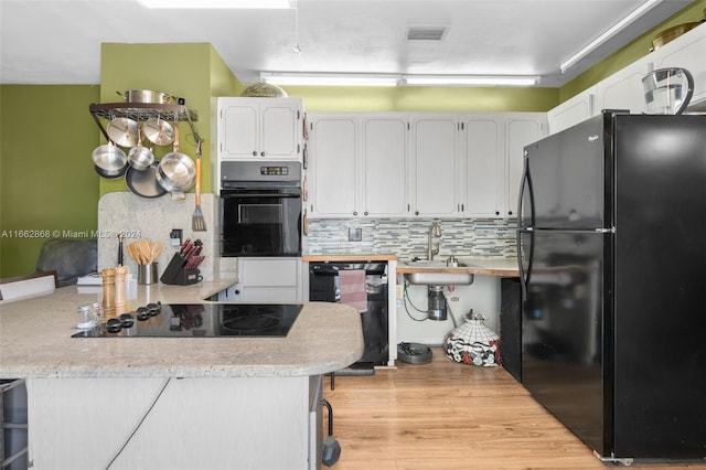 kitchen with white cabinets, black appliances, kitchen peninsula, and light wood-type flooring