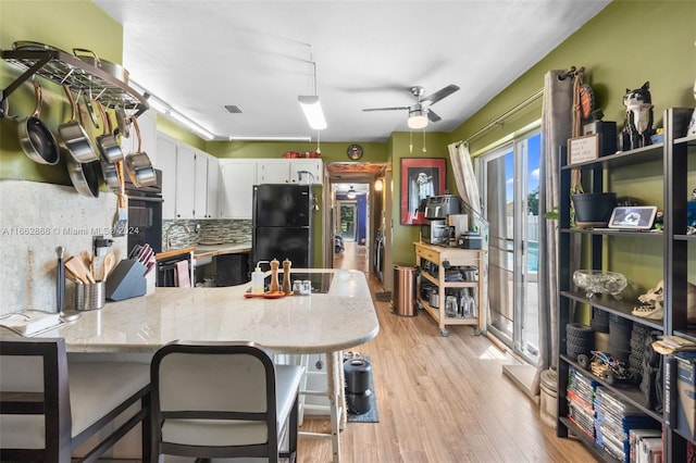 kitchen featuring white cabinetry, kitchen peninsula, black refrigerator, light wood-type flooring, and ceiling fan