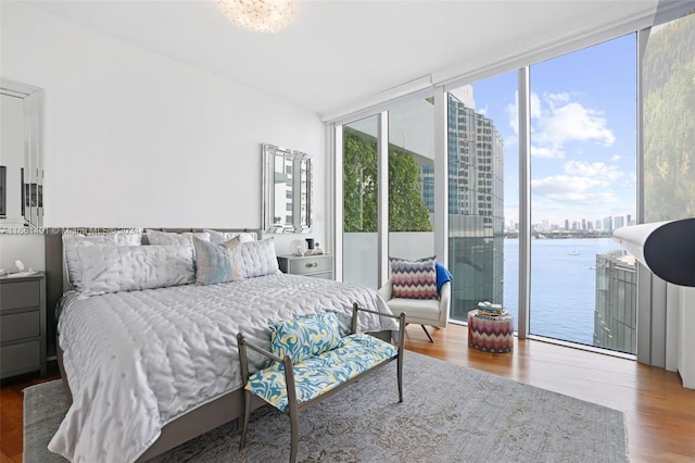 bedroom featuring a wall of windows, wood-type flooring, a water view, and access to outside