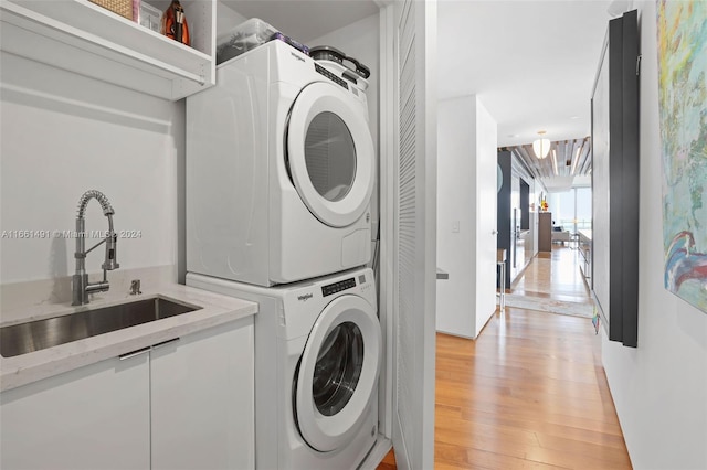 clothes washing area with stacked washer / dryer, sink, and light hardwood / wood-style flooring