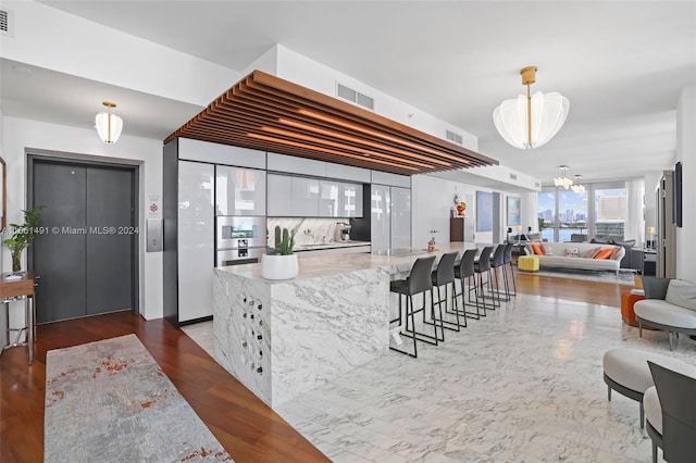 kitchen with dark wood-type flooring, white cabinetry, a kitchen breakfast bar, a notable chandelier, and light stone countertops