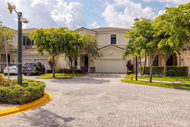 view of front facade featuring a garage, decorative driveway, a tile roof, and stucco siding