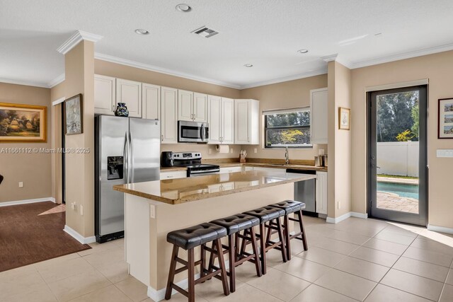 kitchen featuring white cabinets, light stone countertops, ornamental molding, and a center island