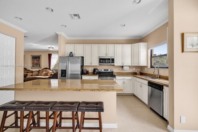 kitchen with a breakfast bar, a center island, white cabinetry, stainless steel appliances, and light stone countertops