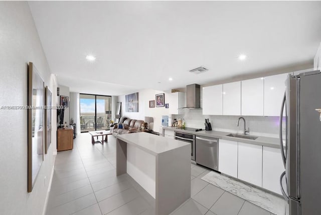 kitchen with appliances with stainless steel finishes, wall chimney exhaust hood, expansive windows, white cabinets, and sink