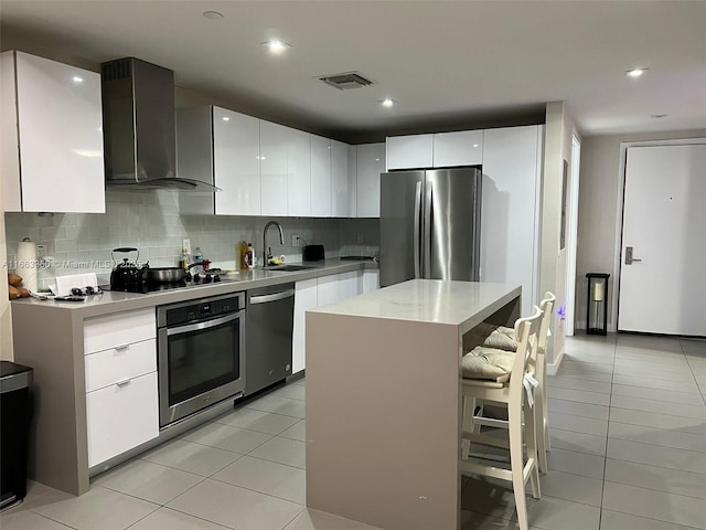 kitchen with visible vents, appliances with stainless steel finishes, light countertops, wall chimney range hood, and a sink