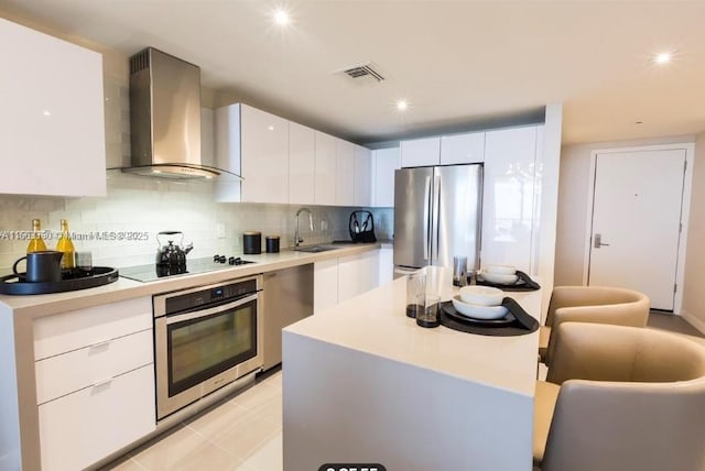 kitchen with stainless steel appliances, tasteful backsplash, light countertops, a sink, and wall chimney exhaust hood