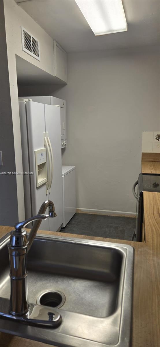 kitchen featuring white cabinetry, sink, wood counters, white refrigerator with ice dispenser, and stacked washer / dryer