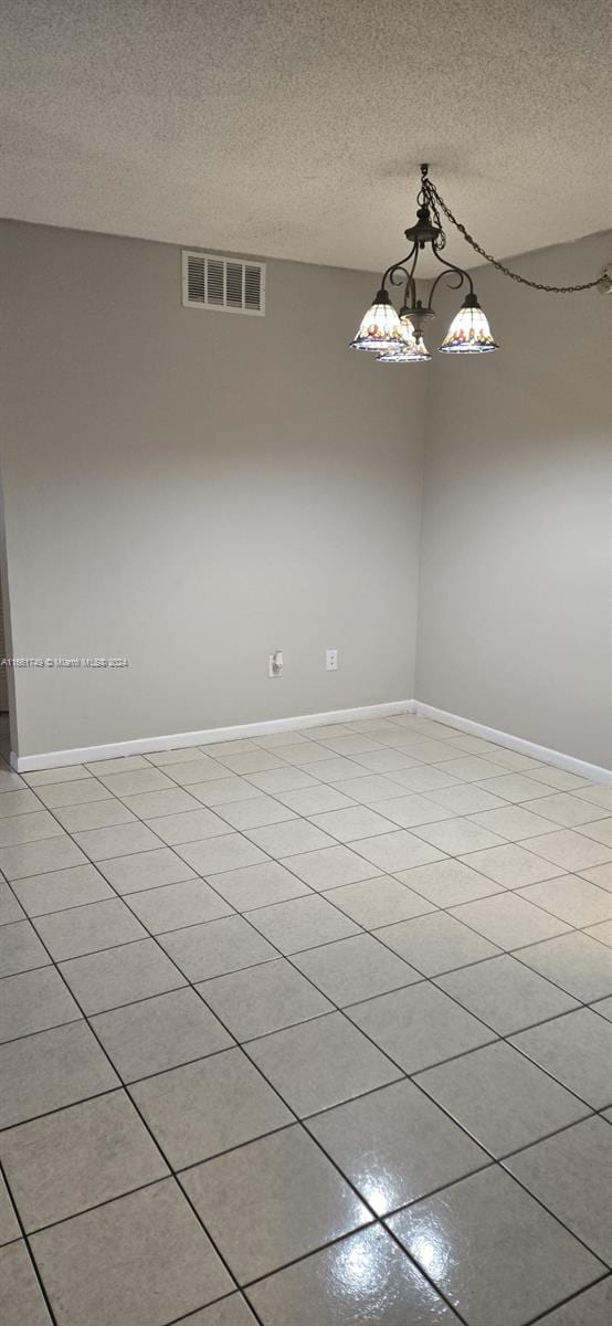 unfurnished room featuring light tile patterned floors, a textured ceiling, and an inviting chandelier